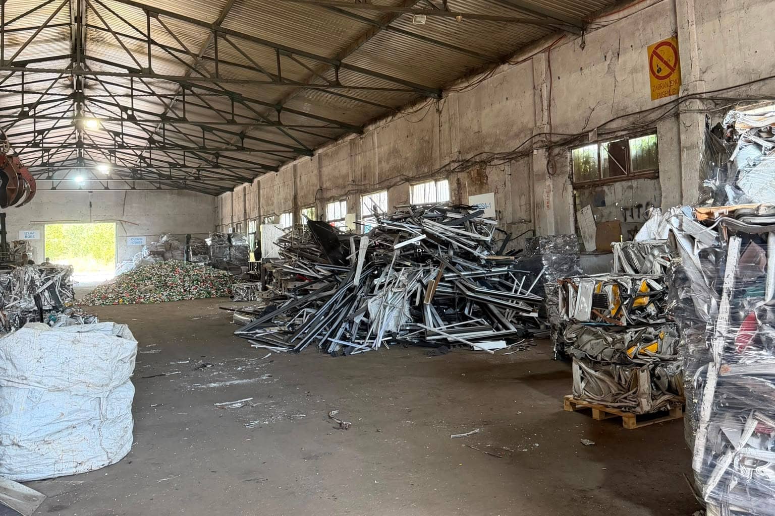 Pogled niz halu, sa hrpom aluminijskih prozorskih profila i baliranim materijalom na paletama