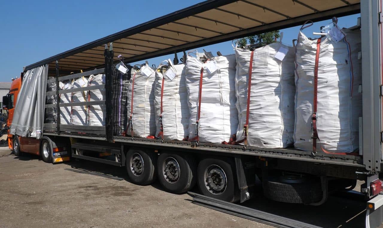 A curtainside trailer loaded with bulk bags of secondary raw material, held by tie-down straps
