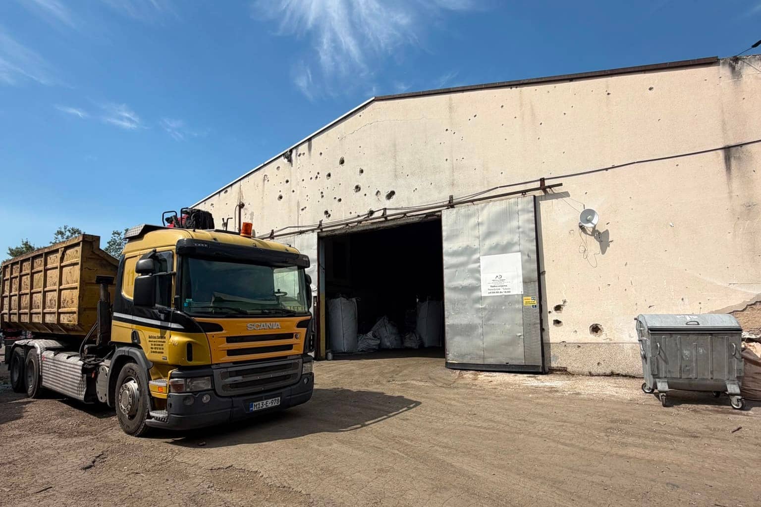 The hall from outside under a clear sky, with a yellow truck and a roll-off container in front of the open door