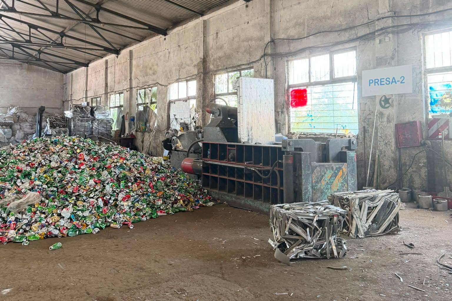 Hidraulična presa označena tablom PRESA-2, uz hrpu limenki i dvije gotove bale aluminija