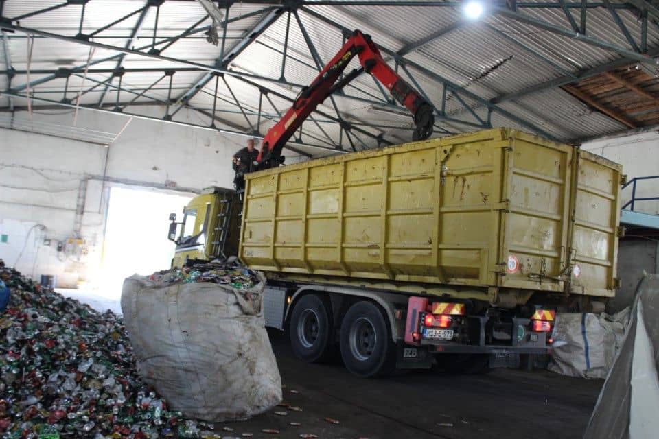 A truck with a hydraulic crane in the hall, beside a bulk bag full of crushed cans